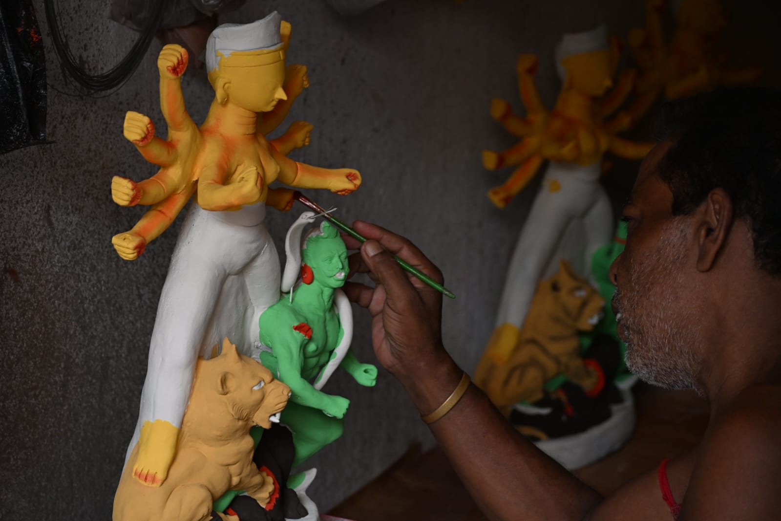 An artisan painting the base colours onto Durga, the lion and Mahishasura