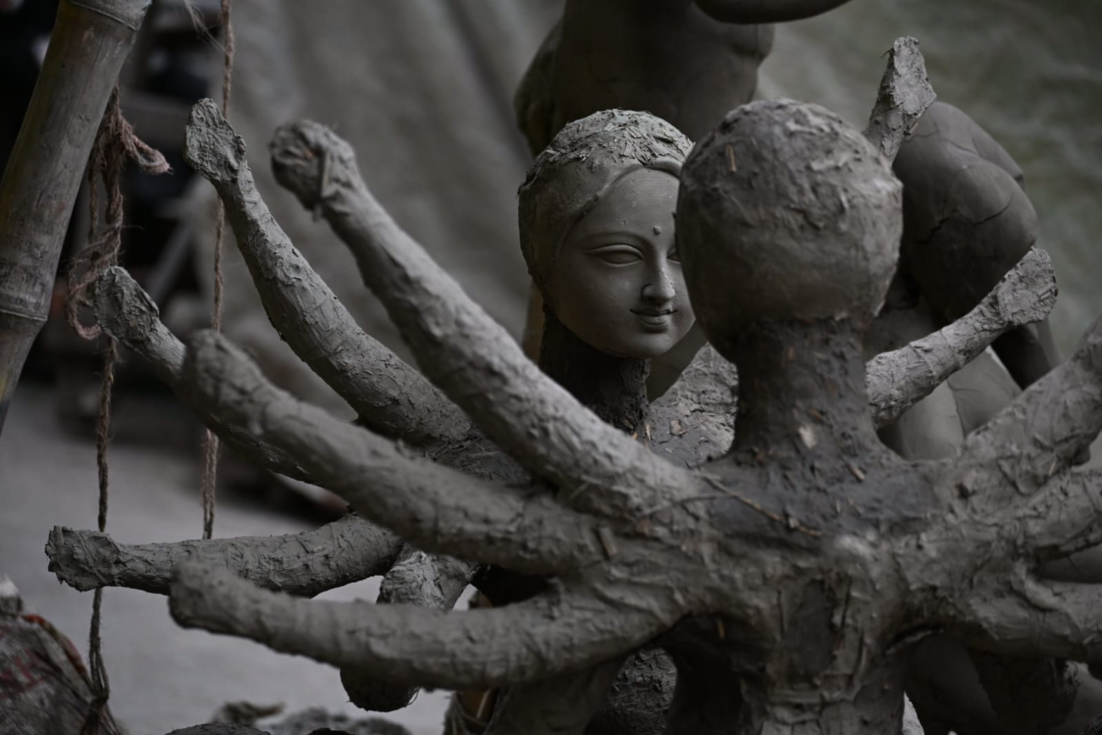 A clay Durga face emerging among unfinished clay arms