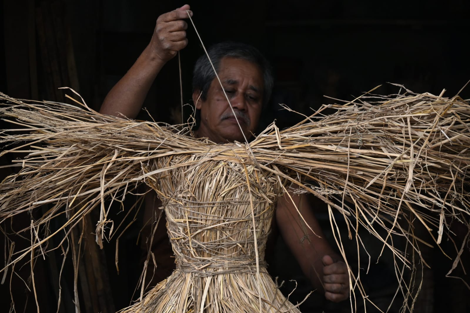 An artisan binding straw into the frame of an image