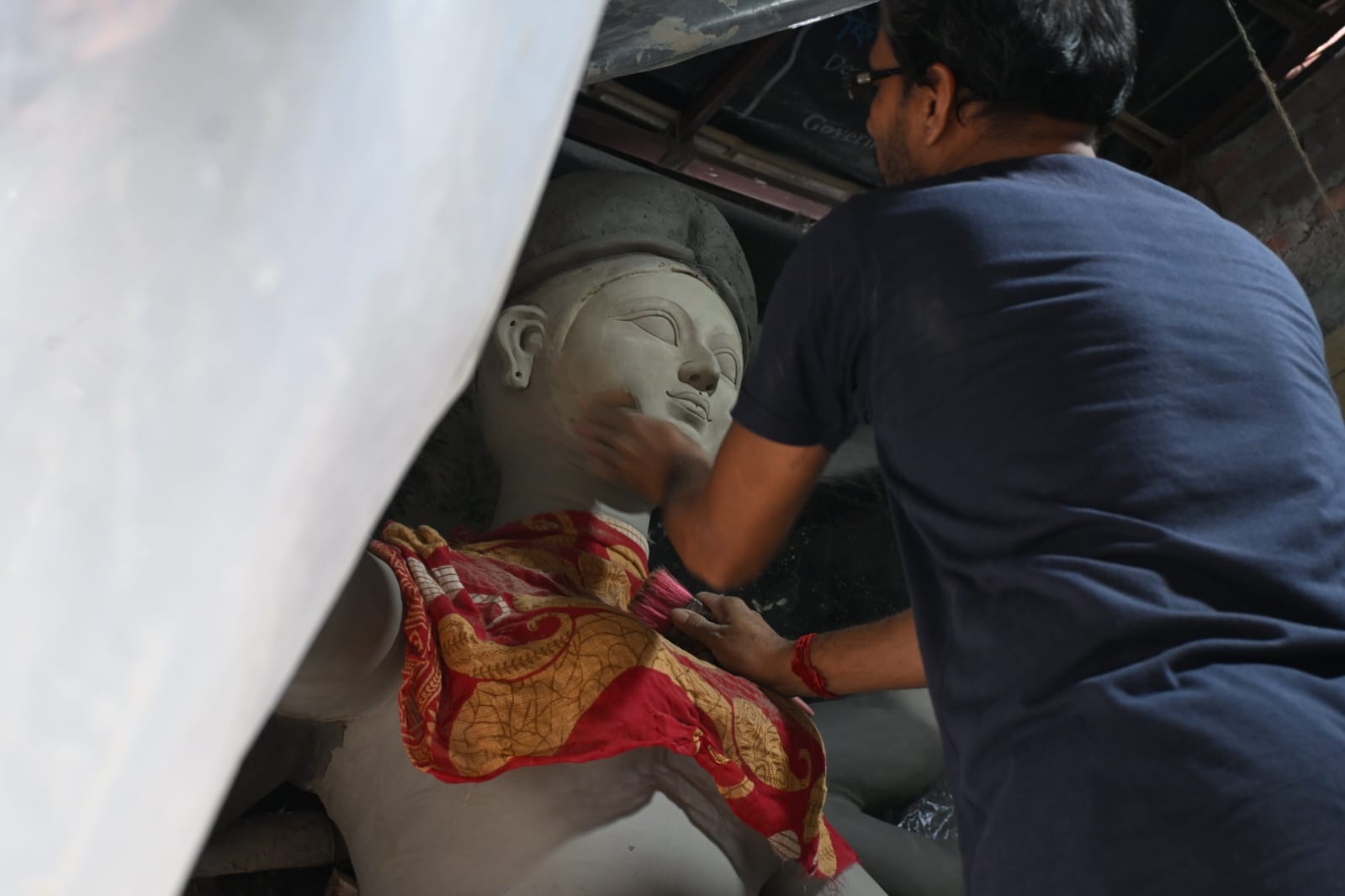 An artisan smoothing the clay face of a large Durga image