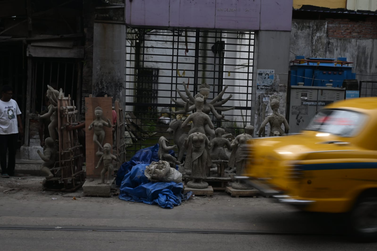 Unfinished clay Durga images on a Kumartuli street as a yellow taxi passes